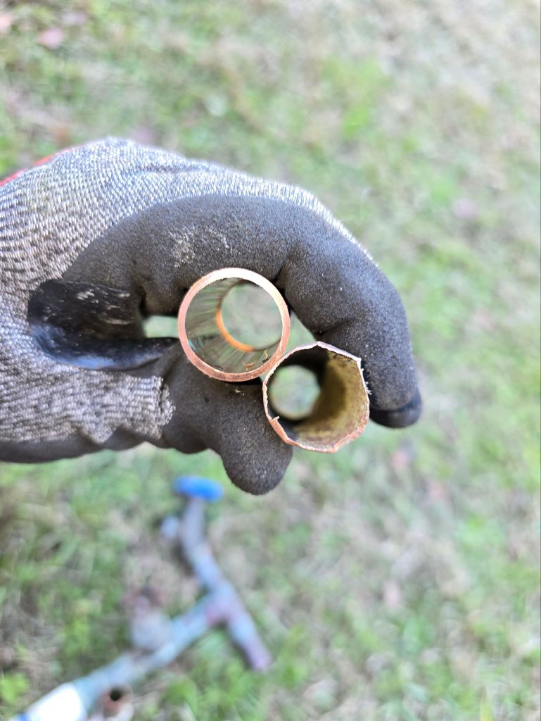 Side-by-side comparison of a severely thinned aging copper water service pipe next to new piping, showing corrosion damage from a Magnolia home built in 1992.