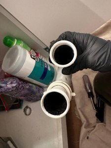 White P-trap pipe turned black from AC condensate sludge buildup causing a clogged drain line in an attic system.