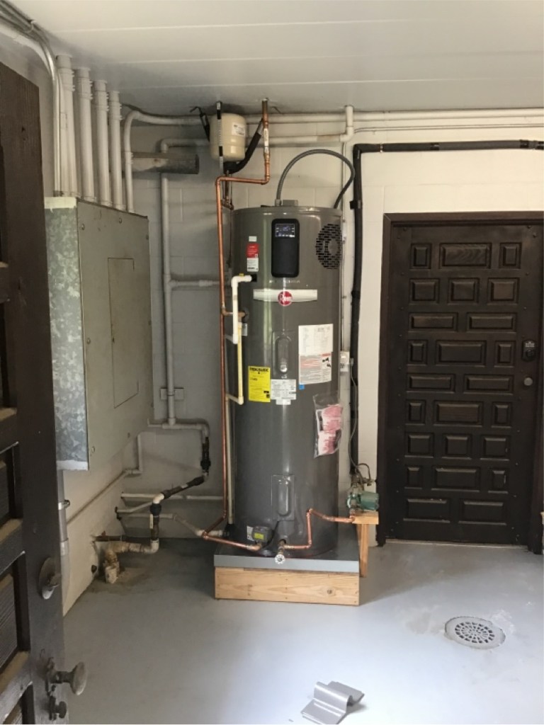 Hybrid electric water heater installed in a garage, designed for energy efficiency and lower operating costs.