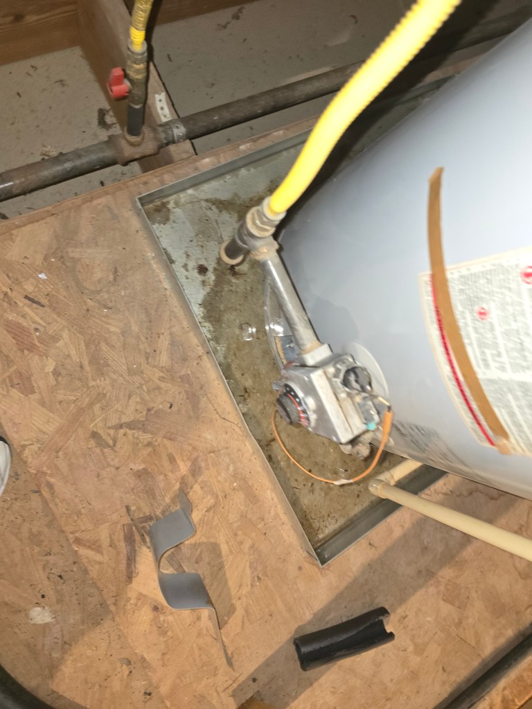 Water collecting in an attic water heater drain pan from a leaking aging tank water heater.